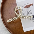 Dettaglio di una pinza per capelli dorata con perle incastonate su vassoio in legno - Croce Perla