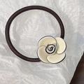 Detail eines eleganten cremefarbenen Kamelienanhängers an einem dunkelbraunen Haargummi - Beige