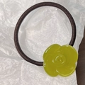 Close-up of a green resin camellia flower charm on an elastic brown hair tie band - Green