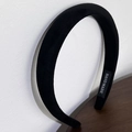 Detail of black velvet padded headband with handmade label on minimalist wooden surface - Black