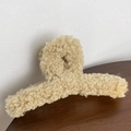 Dettaglio del mollettone in peluche con texture in finta pelliccia riccia su tavolo in legno - Cachi