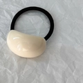 Dettaglio di un ciondolo ovale in resina color crema su un elastico per capelli nero - Crema