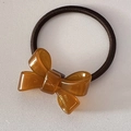 Macro detail of amber resin bow hair tie with golden handmade lettering and elastic band - Coffee
