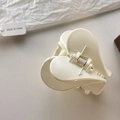 Detail view of a double-layered cream heart hair claw clip with a silver metal spring - Off-white