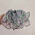 Detail eines Chiffon-Haargummis mit lila Blüten auf hellgrünem Stoff mit Saumkante - Grün