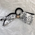 Close-up of French bow hair tie with vintage metal charm and letter print texture - White
