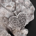 Macro shot of silver vintage heart pendant with intricate filigree texture on grey stone - Silver