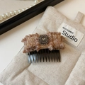 Dettaglio della molletta a fiocco in tweed con diamante grigio su sfondo in tessuto beige - Marrone Rosa Pettine a Incastro