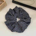 Détail d'un chouchou floral bleu marine en mousseline avec un collier de perles en fond - Floral Bleu