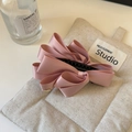 Détail d'une pince à cheveux à nœud en satin rose posée sur un tissu texturé doux - Rose