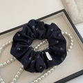 Dettaglio di scrunchie floreale con etichetta Hand Made e collana di perle su vassoio - Blu navy