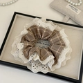 Detail van bruine geruite scrunchie met kanten randen op een minimalistisch dienblad - Lichtkoffie