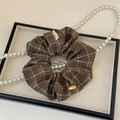 Détail d'un chouchou en tissu à carreaux avec un pendentif doré et une étiquette faite main - Café Foncé