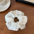 Detailansicht von cremeweißem Chiffon-Haargummi mit Spitzenblumen und Pailletten auf Holz - Scrunchie