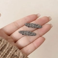 Gros plan de petites barrettes ovales en strass gris foncé sur fond beige doux - Gris Argent