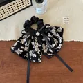 Dettaglio di uno scrunchie floreale con un grande fiocco e accento centrale in perla - Nero Floreale