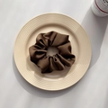 Detailed view of coffee brown satin scrunchie with pleated texture on a plate - Brown