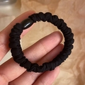 Elastic black scrunchie with oval decorative bead shown on a warm yellow background - Black