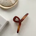 Dettaglio della pinza per capelli opaca color ambra con design elegante a linee intrecciate - Marrone