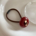 Close-up of deep brown elastic hair tie with red acrylic button and golden metal engraving - Red