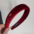 Detail shot of a red velvet padded headband featuring a golden handmade metal label tag - Red