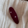 Vue détaillée d'une barrette en feutre bordeaux à pois blancs sur un fond en tissu doux - Rouge Ovale