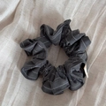 Detailed macro shot of dark grey striped fabric scrunchie on soft beige linen background - Gray