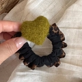 Detail of leopard print scrunchie with a green plush heart charm on beige fabric - Green Heart