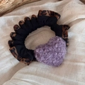 Detail of leopard print scrunchie with a purple plush heart charm on beige fabric - Purple Heart