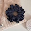 Close-up of dark grey knitted scrunchie with black ruffled edges on beige fabric - Blue