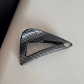 Macro detail of carbon fiber texture and silver metal Hand Made tag on hair claw - Oblique Triangle