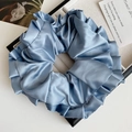 Détail macro d'un grand chouchou en satin plissé bleu clair présenté dans un coffret - Bleu Brume
