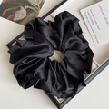 Gros plan d'un chouchou géant en satin noir avec texture plissée sur un plateau de bijoux - Noir