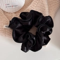 Detail of black satin scrunchie with silver glitter and white woven egg brand label - Black