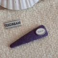 Dettaglio della molletta in tessuto viola con etichetta bianca hour su fondo in peluche - Stile Triangolo Lettera Ovale Tessuto Viola