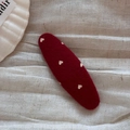 Detailed view of a matte red hair clip with golden heart patterns on white fabric - Red Oval Clip-Heart