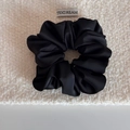 Détail d'un chouchou en satin noir avec texture lisse et plis élégants sur tissu - Noir