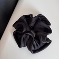 Detail shot of a black satin scrunchie showing glossy ruffled texture and high-quality fabric - Black