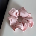 Close-up of soft pink satin scrunchie with silky texture and ruffled edges for hair styling - Pink