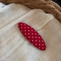 Détail d'une pince à cheveux rouge à pois blancs sur fond en tissu rustique - Design Ovale / Rouge à Pois