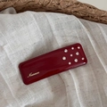 Detail einer roten Emaille-Haarklammer mit goldenem Nuance-Logo und Strasssteinen - Rotes Rechteck