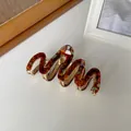 Detail van golfvormige acetaat haarklem met bruine ambertextuur en gouden metalen basis - Amber