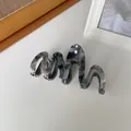 Detailopname van marmeren acetaat haarklem met zilveren metalen tanden en golvend ontwerp - Inktgrijs
