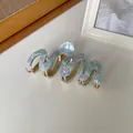 Detail van lichtblauwe marmeren acetaat haarklem met gouden metalen tanden en golvend design - Waterlicht Blauw
