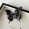 Detailed macro shot of 3D layered black butterfly hair clip with silver glitter accents - Black
