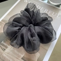 Detailed texture of a black organza oversized scrunchie on a magazine page - Black