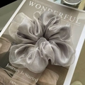 Detailed texture of an oversized silver-grey organza scrunchie on a fashion magazine - Gray