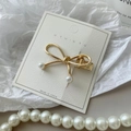 Dettaglio del fermaglio per capelli a fiocco dorato con perle bianche su carta bianca - Fiocco d'Oro