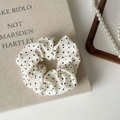 Detailaufnahme des cremefarbenen Punkte-Haargummis mit Spitze auf dekorativem Buch - Scrunchie