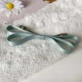 Close-up of light blue satin bow hair clip with silver metal alligator base on white fabric - Light Green